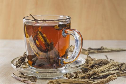 Glass cup of herbal detox tea with visible roots and dried herbs, symbolizing natural cleansing and liver support through plant-based remedies.