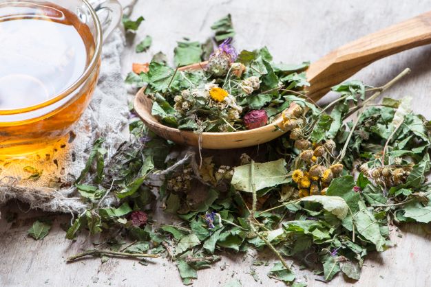 Herbal detox ingredients including dried flowers and leaves, wooden spoon, and glass of tea; natural elements used in holistic cleansing and cellular detox rituals.